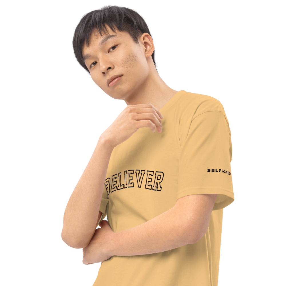 Young man wearing a yellow tee with 'BELIEVER' graphic, showcasing motivational fashion in premium organic cotton.